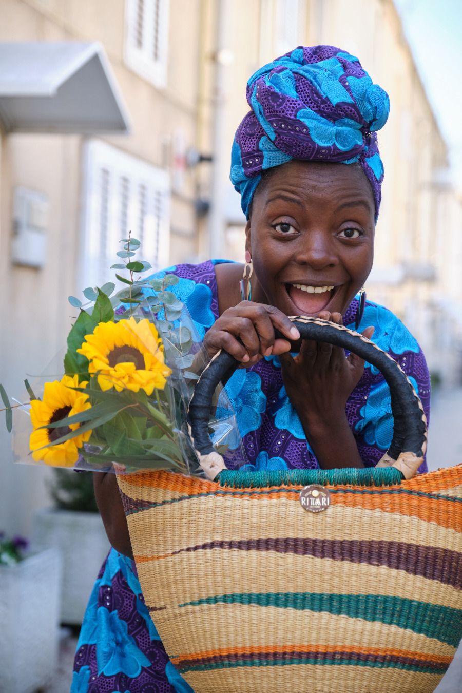 A smiling Black women with a bolgatanga bags and sunflowers.